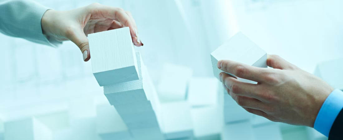 Hands of two business people stacking white toy blocks