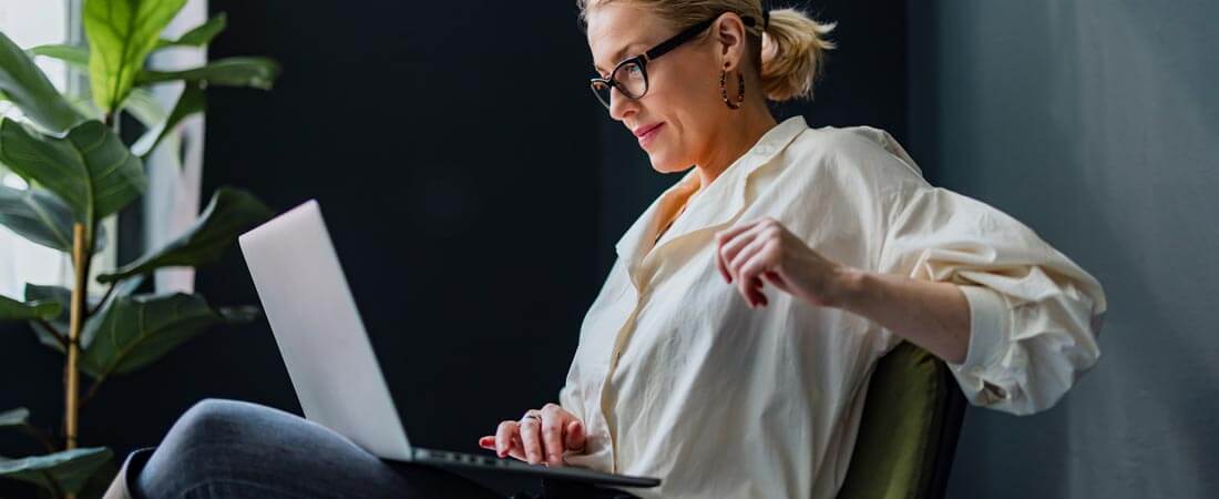 Smiling businesswoman sitting on a chair and typing business report on a laptop keyboard.