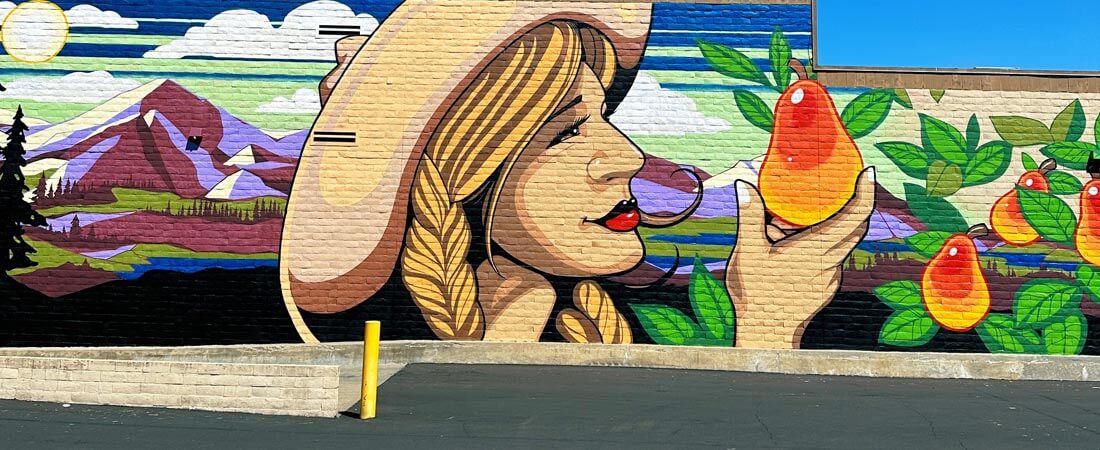 large brightly colored painting on the side of a building of a woman picking a pear